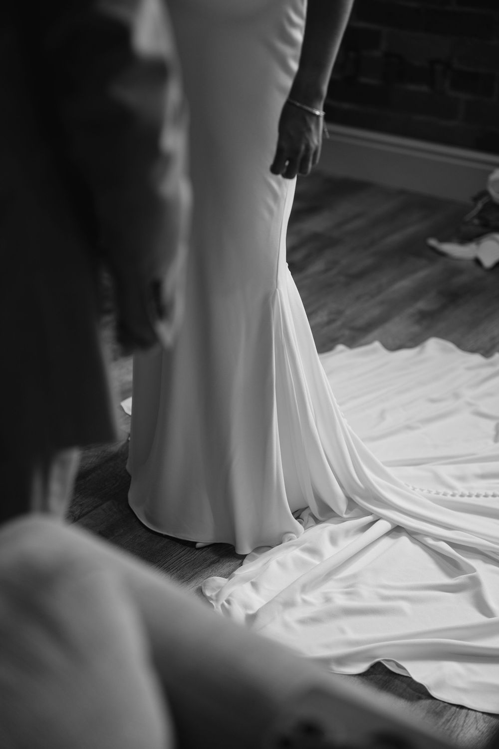 Black and white photo of a bride in a sleek fitted wedding gown with a long train on a hardwood floor.