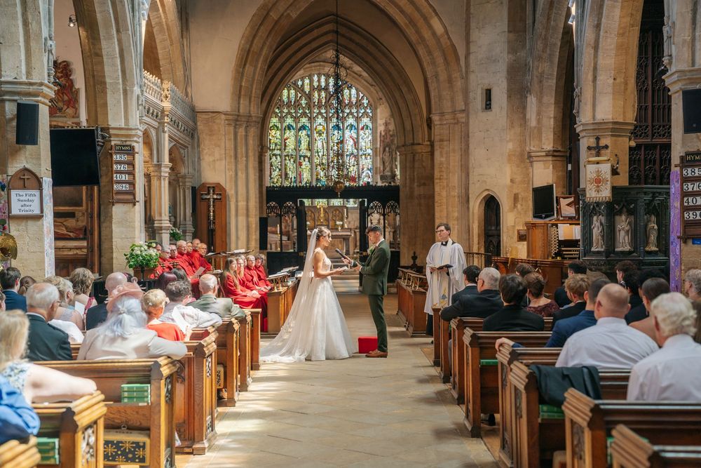 A bride and groom exchange vows at the altar of a historic stone church with stained glass windows. warwickshire wedding photographer
