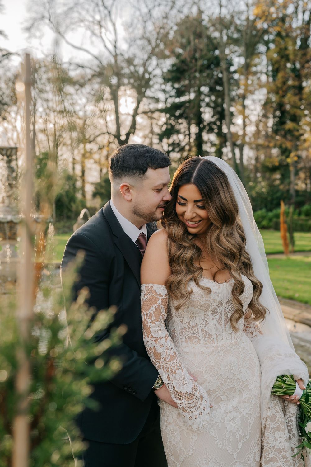 Romantic wedding couple embraces in a scenic outdoor forest setting with autumn trees in the background.