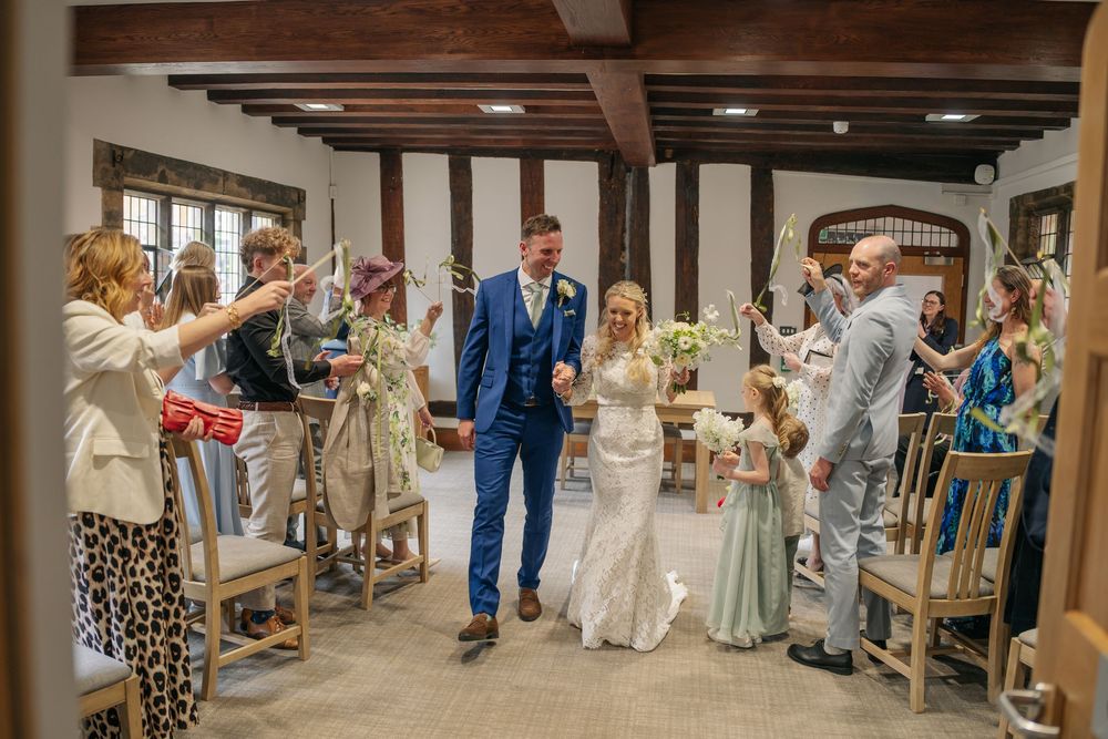 Newlywed couple walks down the aisle as guests celebrate with confetti in a rustic wedding venue. warwickshire wedding photographer