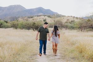 Couple walking hand in hand on desert trail with mountains in background.