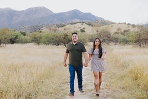 Couple strolling together on dirt path with mountain landscape behind them.