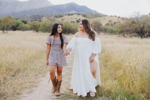Two people walking together on desert path wearing floral dress and white gown.