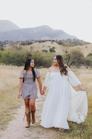 Two people walking and laughing together on desert trail wearing contrasting dresses.