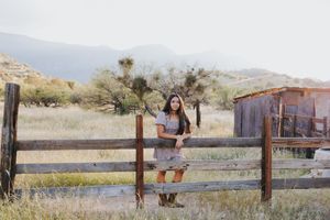 Person in floral dress leaning on wooden fence with desert mountains in background.
