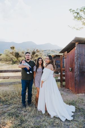 Family photoshoot in rustic desert setting with mountains and wooden barn structures in background.