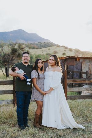Family gathering for photos in desert landscape with mountains and wooden structures visible.