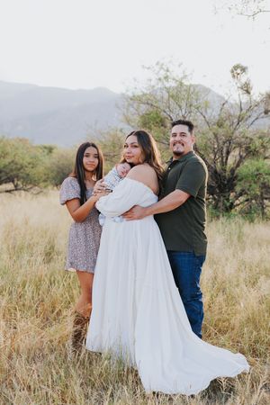 Family portrait in a desert field with mountains, featuring a flowing white dress against golden grass.