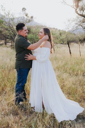 Romantic desert photoshoot with couple in white dress and green shirt against mountain backdrop.