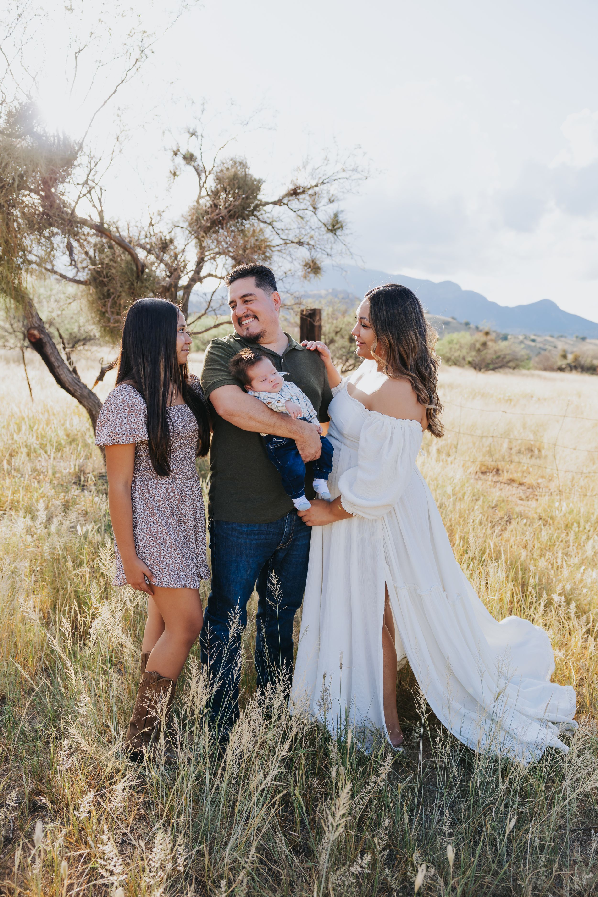 Family photoshoot in a desert landscape with mountains and tall grass at sunset.