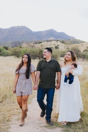 Family walking together on desert path with mountains and blue sky in background.