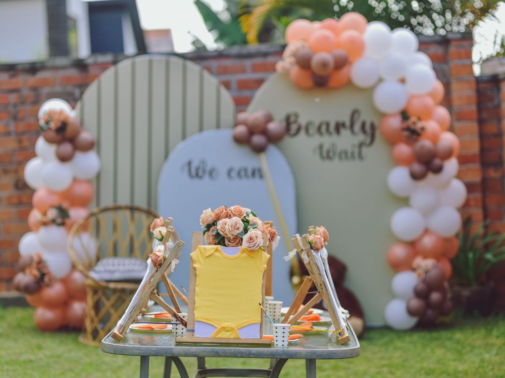 Baby shower decoration with peach and white balloon arch and teddy bear theme.