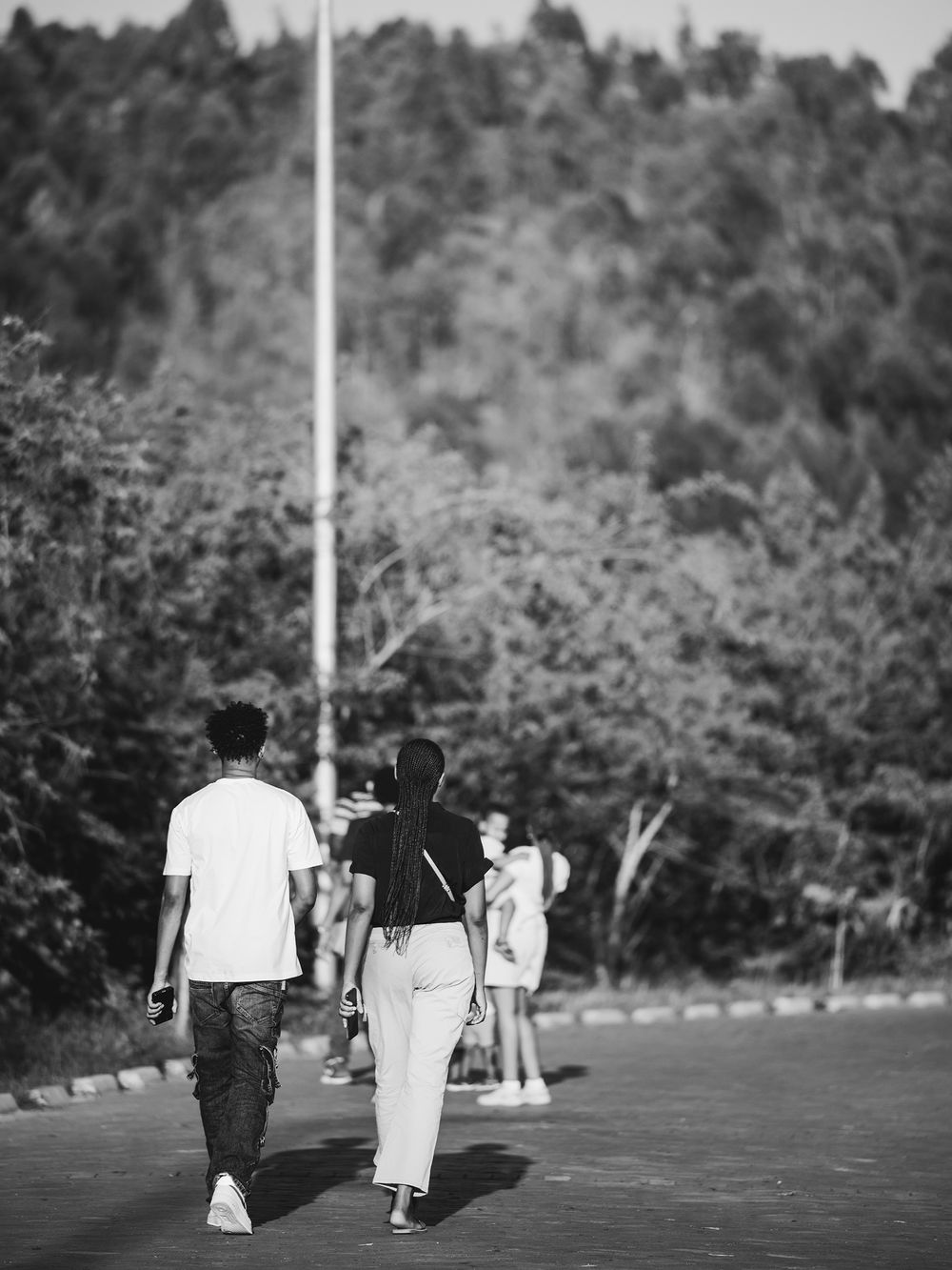 Black and white photograph of people walking on a path with forested hills in background.