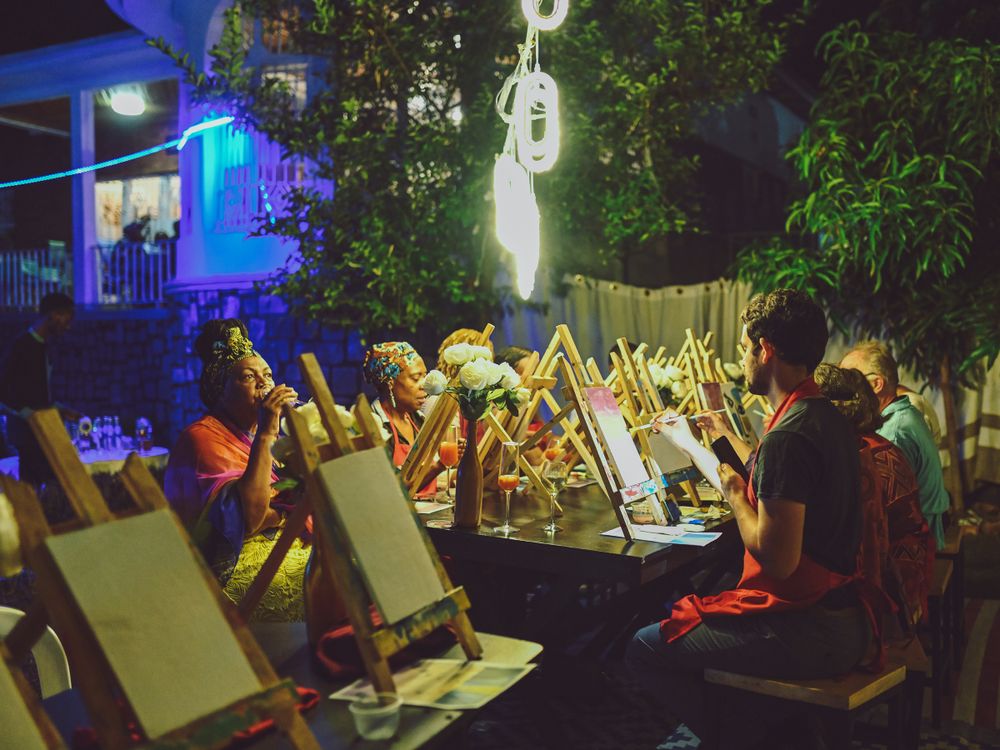 Nighttime paint and sip party with artists working at easels under outdoor lighting.