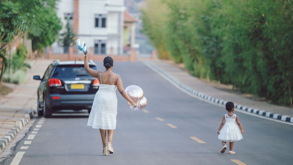 A parent and child in white dresses walking together on an empty suburban street.