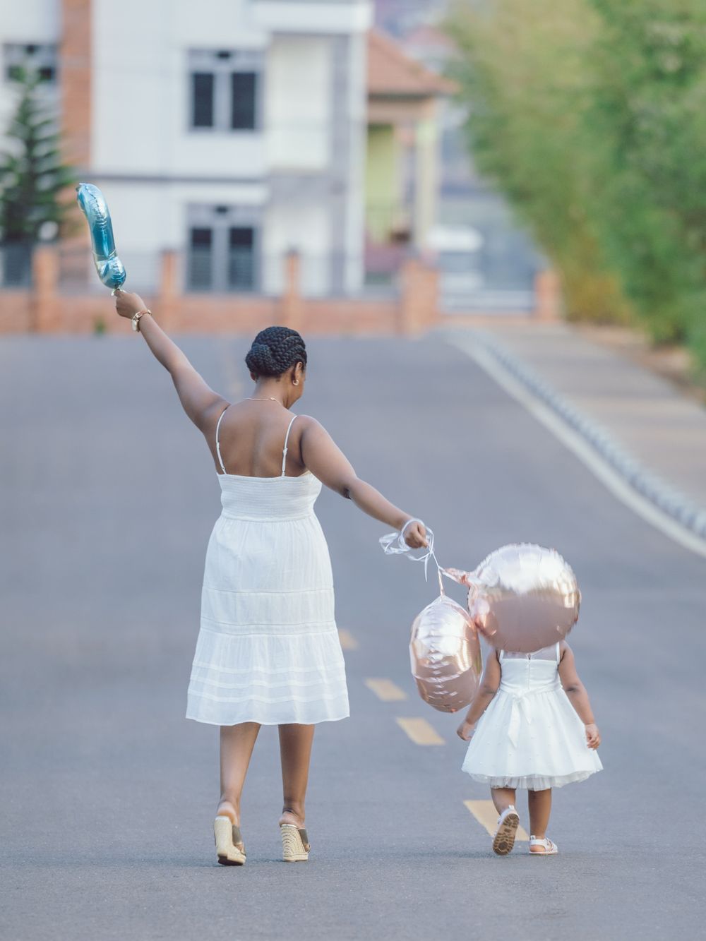 A parent and child holding hands while walking down a street in matching white dresses.