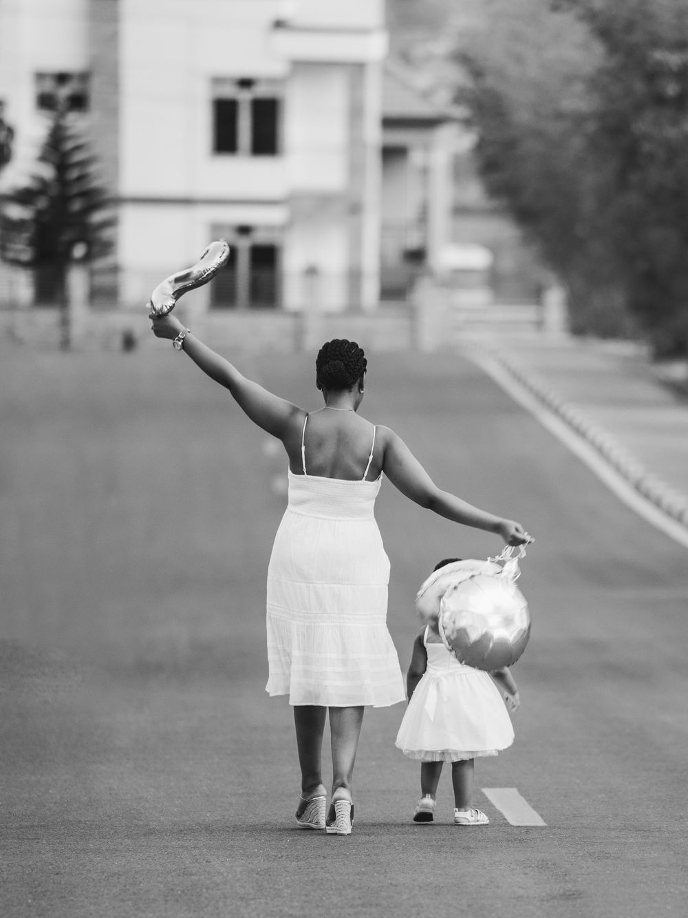 A black and white photo of two figures in white dresses walking down a residential street.