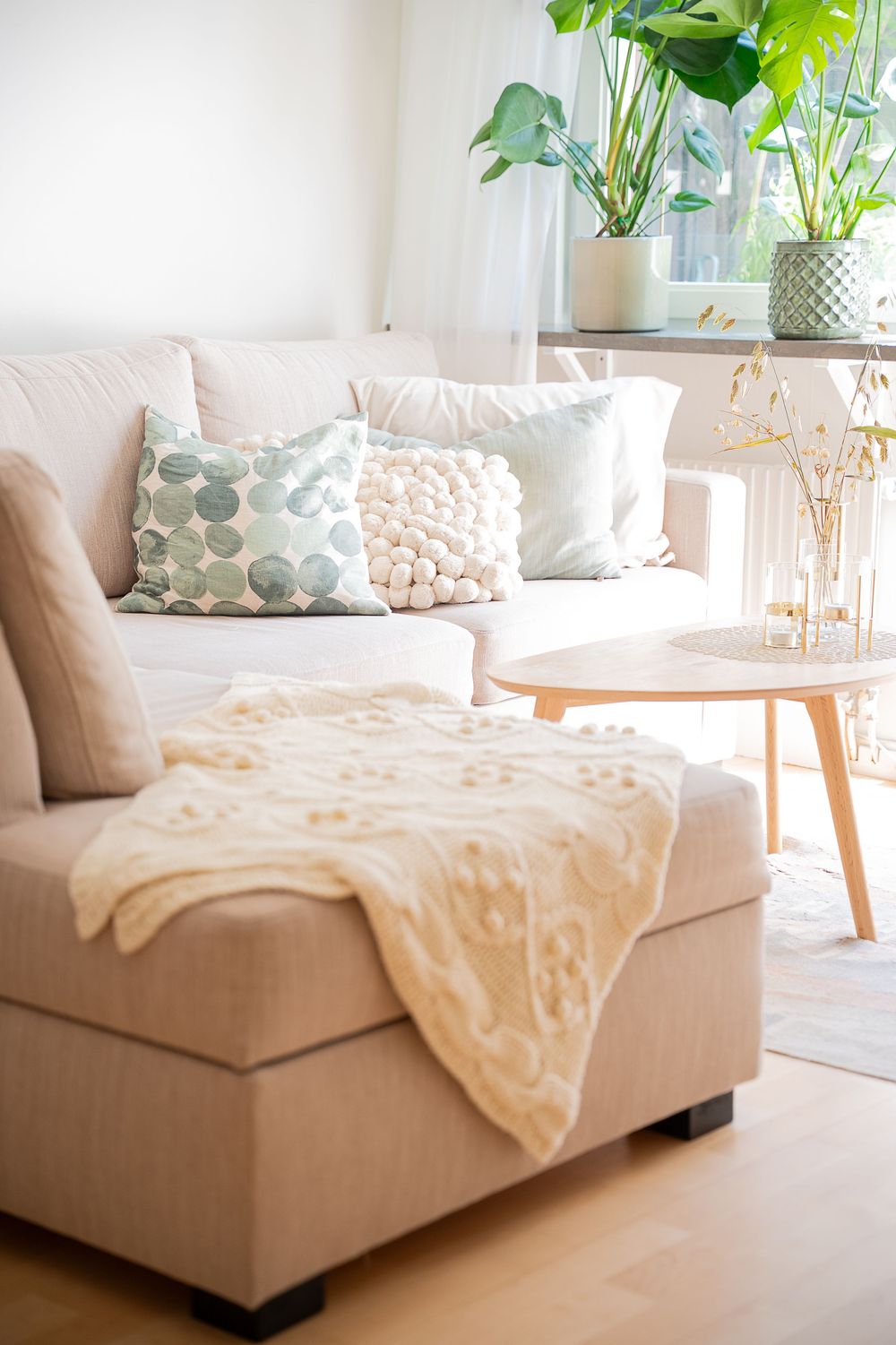 A series of five sliding images showing a beige sectional sofa with throw pillows and blankets in a bright sunlit room.