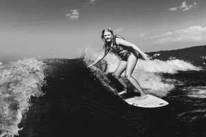 A surfer in a bikini rides a wave in black and white photography.