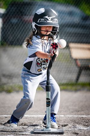 Young baseball player in white uniform and helmet readies stance during close-up sequence at home plate.