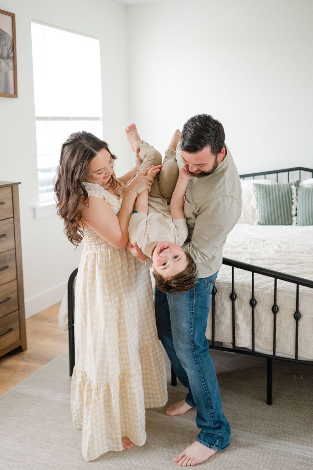 Family sharing playful moment with baby in bright white room with metal bed frame.