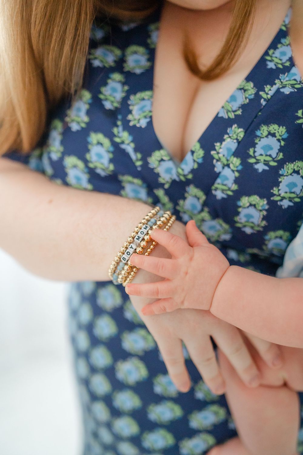 Close-up of hands with jewelry against floral blue dress pattern.