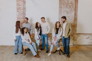 Casual group photo session against white brick wall in studio setting.