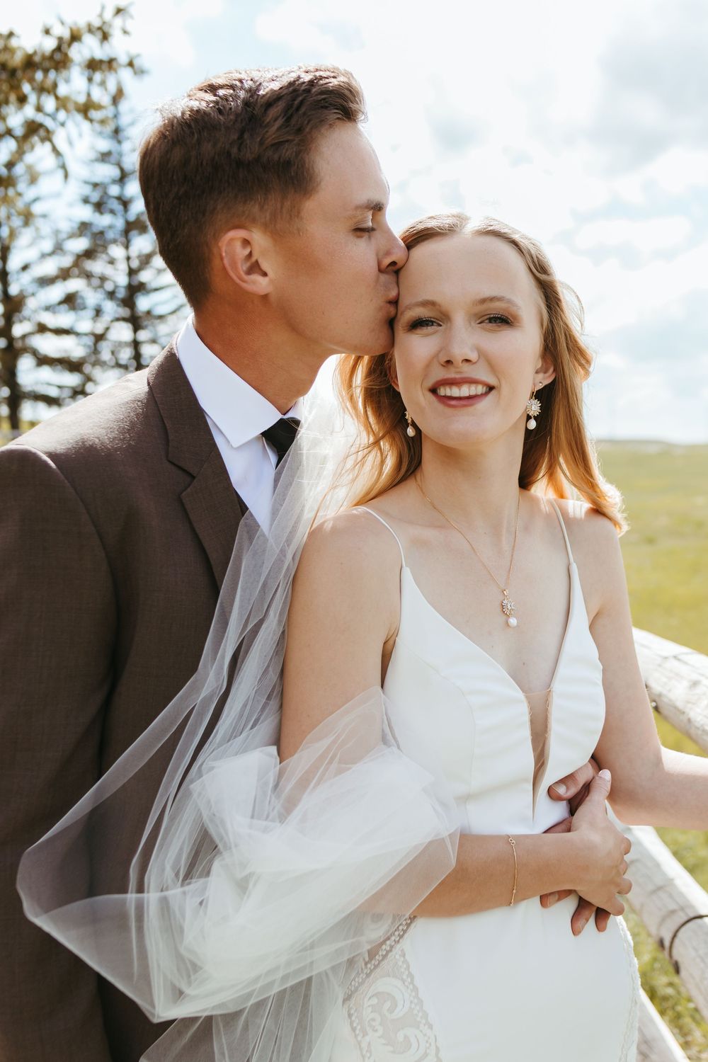 Romantic wedding photoshoot in natural outdoor setting with flowing white veil and sunlit backdrop.
