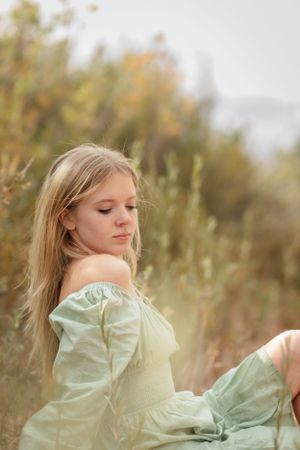 Person in vintage mint green dress poses thoughtfully in autumn field.