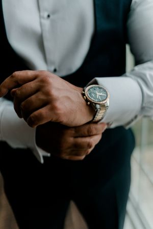 Close-up shot of hands adjusting an elegant silver and blue wristwatch while wearing formal attire.