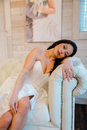 A woman in a white flowy gown reclines elegantly on a modern studded couch in a bright interior setting.