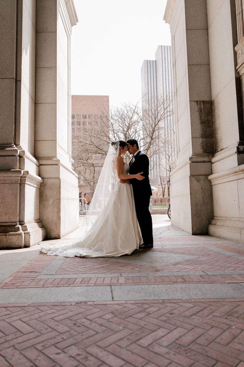 Bride and groom share a romantic kiss between grand stone columns at an elegant outdoor wedding venue.