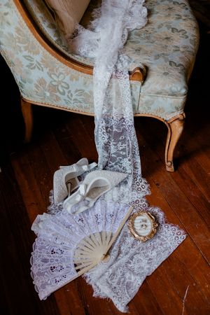 Delicate white lace fan and fabric accessories arranged on a wooden floor in a vintage style display.
