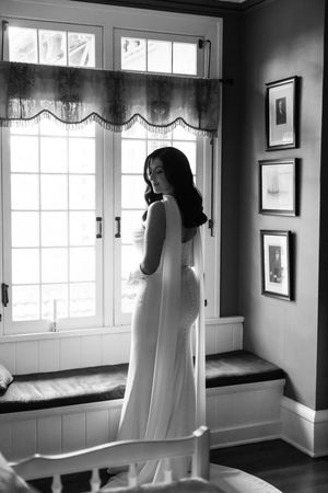 Black and white photograph of window-lit room with white curtains creating ethereal, ghost-like shapes.