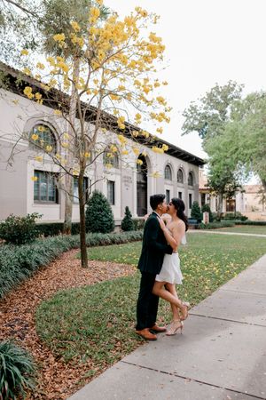 Couple sharing romantic moments in autumn setting outside historic white building with falling leaves on sidewalk.