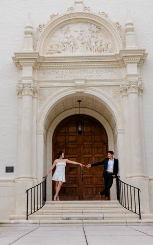 Couple poses creatively in front of ornate white stone church entrance with dramatic architectural details.
