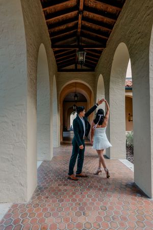 Couple dancing and twirling in a Spanish colonial style covered walkway with white pillars and terracotta tile floors.