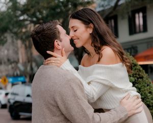 A romantic couple embraces and shares an intimate moment outdoors on a sunny day.