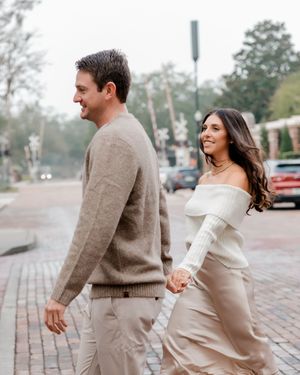 A couple in neutral toned outfits dance playfully on a brick paved street during a photo session.