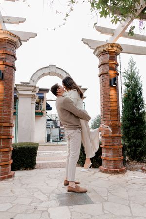 A couple shares a romantic dance dip under an outdoor pergola with brick columns and stone flooring.
