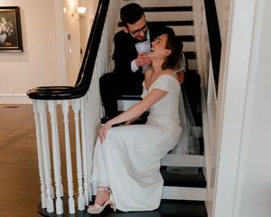 A couple shares a romantic dance in an elegant white room with a staircase and chandelier.