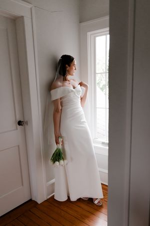 A bride in a white dress stands by a window in a minimalist room, shown in a series of artistic wedding portraits.