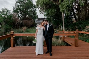 A couple walks together across a wooden bridge in an outdoor garden setting during a wedding ceremony.