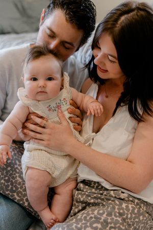 A baby in a white dress rests on a leopard print pillow while being held by someone in a white shirt.