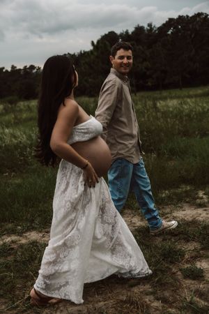 A couple in casual attire walks together through a grassy field on a cloudy day.