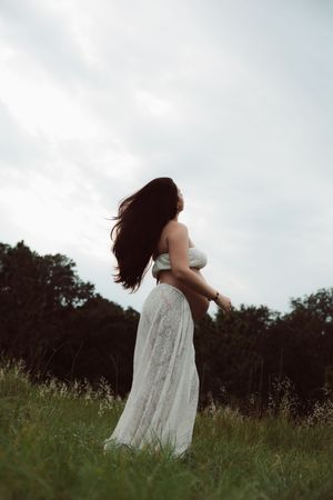 A person in a flowing white dress spins gracefully through a wild meadow on an overcast day.