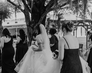 A black and white photo series showing a wedding celebration with guests gathered under trees.