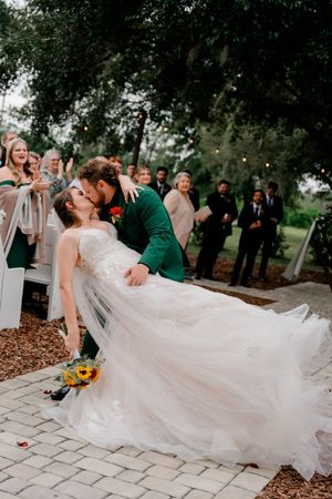 A romantic dip dance pose between a couple in wedding attire on a stone patio with guests watching in the background.