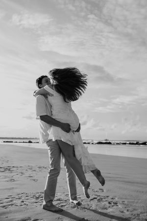 Romantic black and white photo series showing a couple embracing and dancing on a beach at sunset.