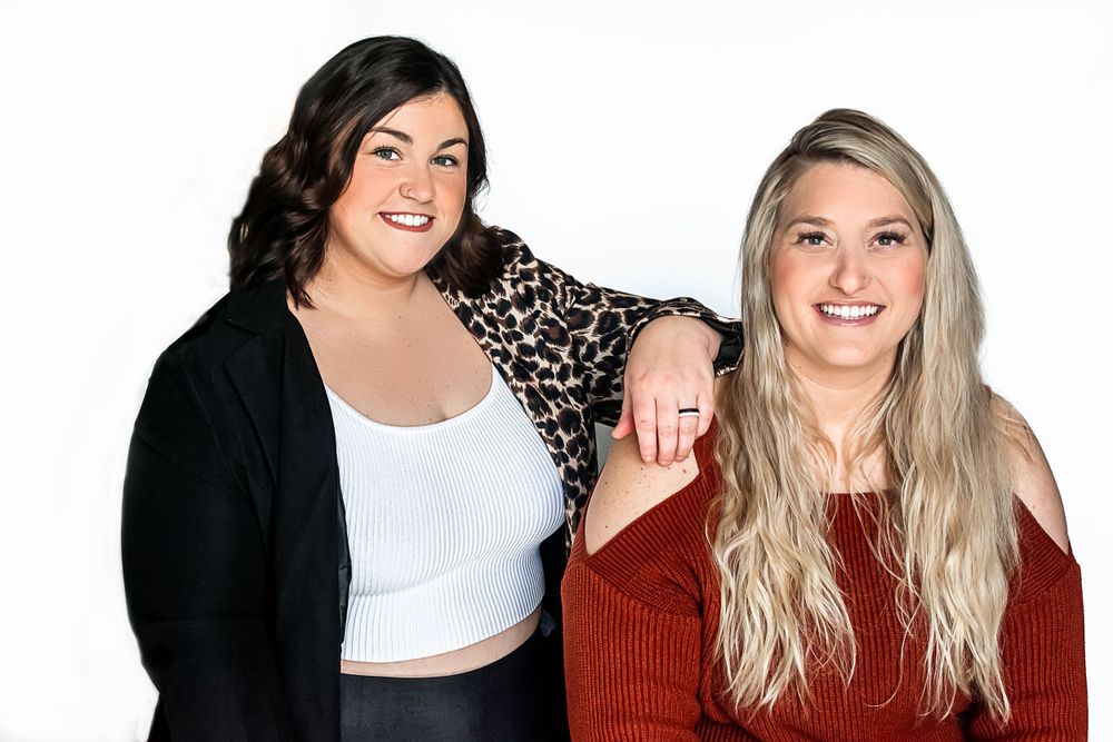 Two women wearing casual clothing and smiling together against a white background.